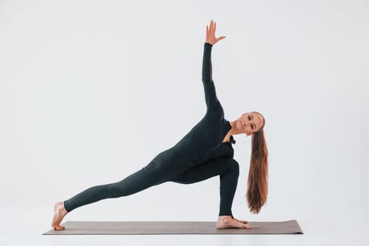 Side view. Young woman in sportive clothes doing gymnastics indoors.