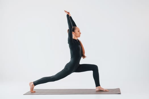 Side view. Young woman in sportive clothes doing gymnastics indoors.