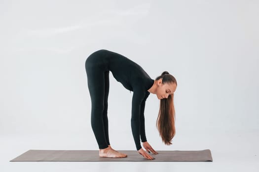 In black clothes. Young woman in sportive clothes doing gymnastics indoors.