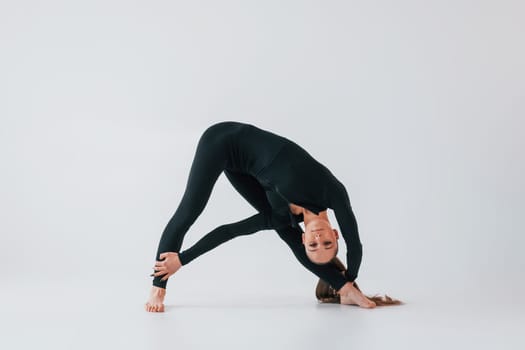 In black clothes. Young woman in sportive clothes doing gymnastics indoors.