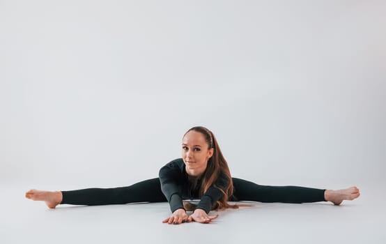In black clothes. Young woman in sportive clothes doing gymnastics indoors.