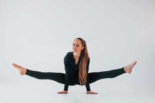 In black clothes. Young woman in sportive clothes doing gymnastics indoors.