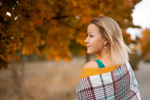 autumn woman in a green dress, plaid, against the background of an autumn tree.