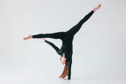 Professional exercises. Young woman in sportive clothes doing gymnastics indoors.