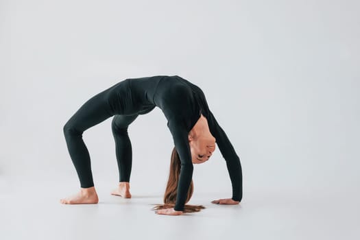 Against white background. Young woman in sportive clothes doing gymnastics indoors.