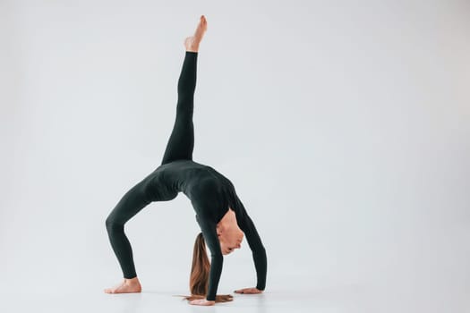 Against white background. Young woman in sportive clothes doing gymnastics indoors.