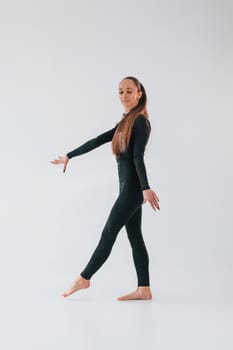 Against white background. Young woman in sportive clothes doing gymnastics indoors.