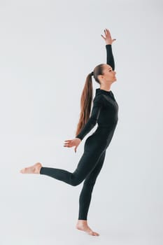 White background. Young woman in sportive clothes doing gymnastics indoors.