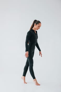 Standing in the studio. Young woman in sportive clothes doing gymnastics indoors.