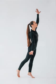 Standing in the studio. Young woman in sportive clothes doing gymnastics indoors.