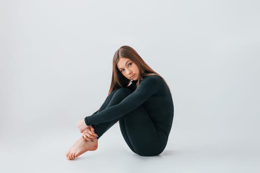 On the floor. Young woman in sportive clothes doing gymnastics indoors.