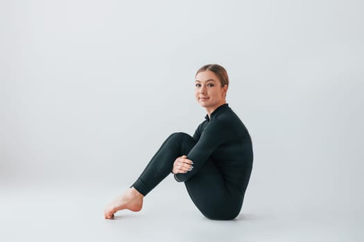View from the side. Young woman in sportive clothes doing gymnastics indoors.