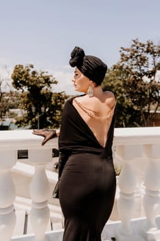 Stylish woman in the city. Fashion photo of a beautiful model in an elegant black dress posing against the backdrop of a building on a city street.