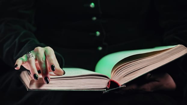 Hands of black witch woman turns over pages of old magic book. Magician learns spells, rituals, esoteric halloween cosplay concept. High quality photo