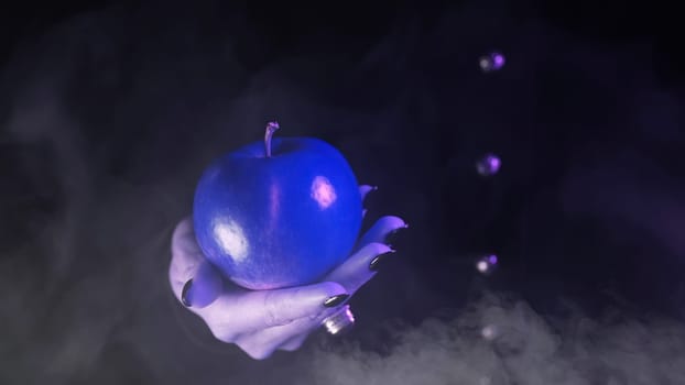 Woman as witch offers blue apple as symbol of toxic temptation, poison, sin. Fairy tale, white snow wizard concept. Spooky halloween, cosplay. Smoke, haze background. High quality photo