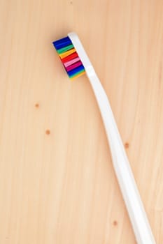 White toothbrush with multicolored bristles on a wooden table. Bristles in all colors of the rainbow. Rainbow toothbrush with white knob. Fashionable oral care.
