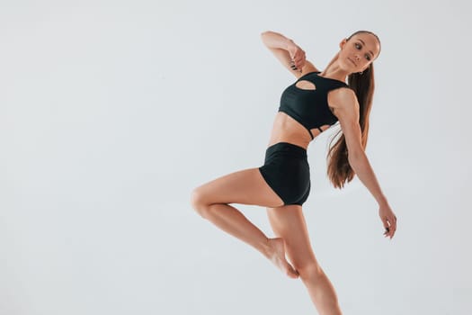 In the studio against white background. Young woman in sportive clothes doing gymnastics indoors.