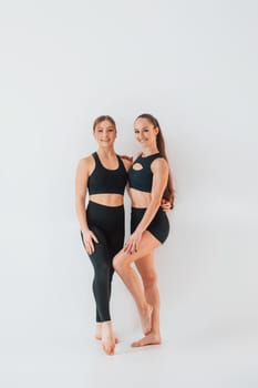 Two young women in sportive clothes is together indoors against white background.