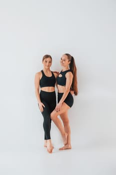 Two young women in sportive clothes is together indoors against white background.