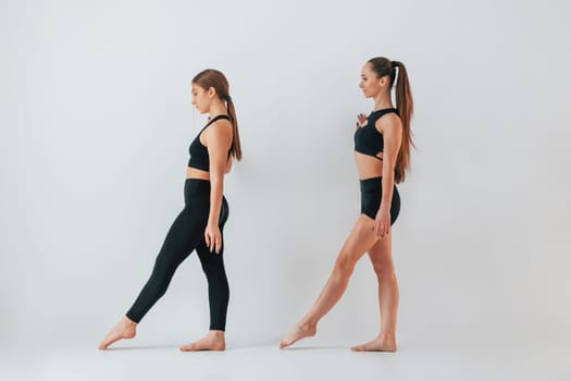 Two young women in sportive clothes is together indoors against white background.