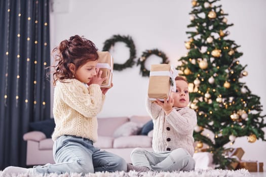 With gift boxes. Little brother and sister is at christmas decorated room together.