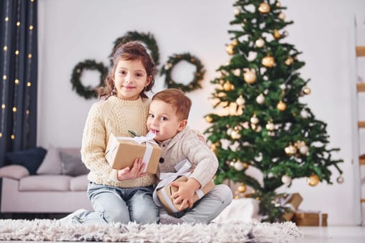 With gift boxes. Little brother and sister is at christmas decorated room together.