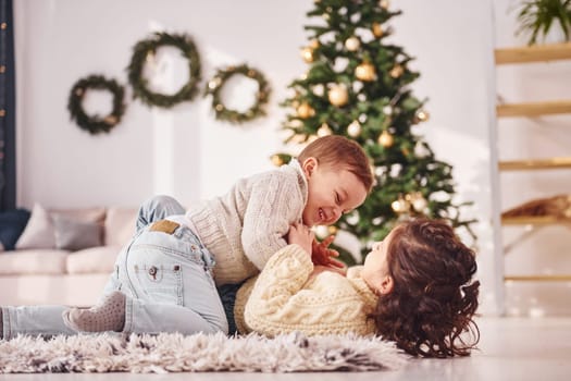 Laying down and playing. Little brother and sister is at christmas decorated room together.