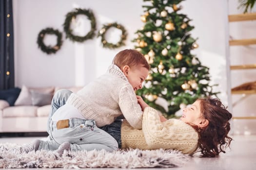 Laying down and playing. Little brother and sister is at christmas decorated room together.