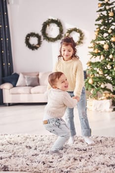 Active time spending. Little brother and sister is at christmas decorated room together.