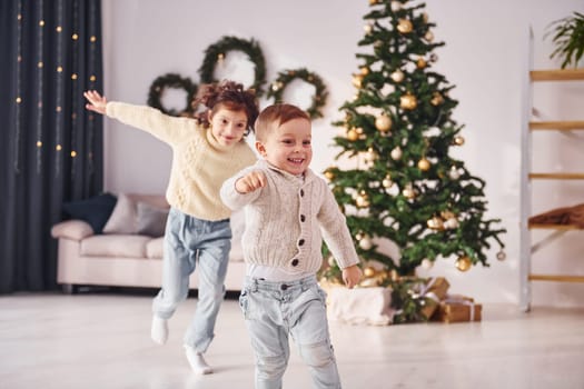 Active time spending. Little brother and sister is at christmas decorated room together.