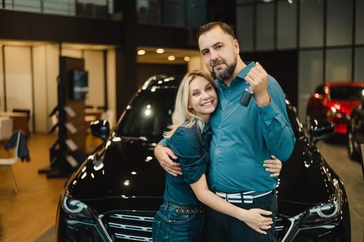 Happy caucasian couple hugging and man holding new car keys in car showroom