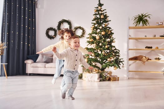 Running together. Little brother and sister is at christmas decorated room.