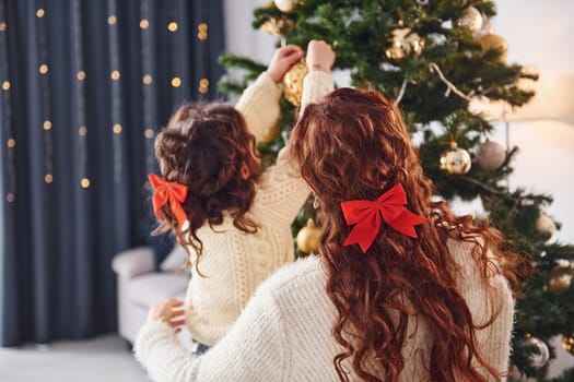 Decorating tree. Mother with her little daughter is at home.