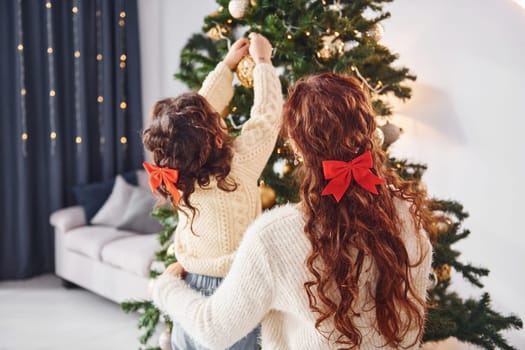 Rear view. Mother with her little daughter is at home. Christmas decorations.