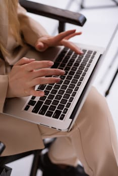 A business woman in a suit is working, typing on a laptop close-up and sitting on a chair. Close-up of hands with computer