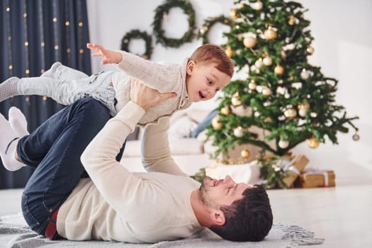 Father having fun with his son indoors in the christmas decorated domestic room.