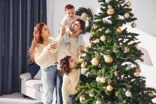 Decorating christmas tree. Family celebrating new year with their children at home.