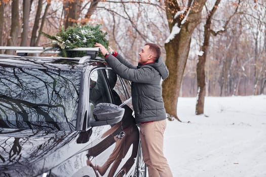 Preparing for the weekend. Man with little green fir is outdoors near his car. Conception of holidays.