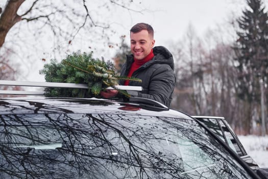 Preparing for the weekend. Man with little green fir is outdoors near his car. Conception of holidays.