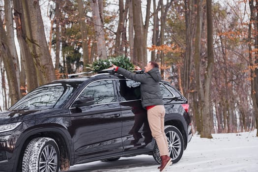 Preparing for the weekend. Man with little green fir is outdoors near his car. Conception of holidays.