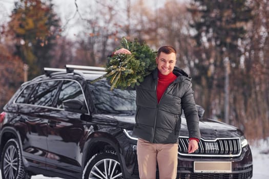 In the forest. Man with little green fir is outdoors near his car. Conception of holidays.