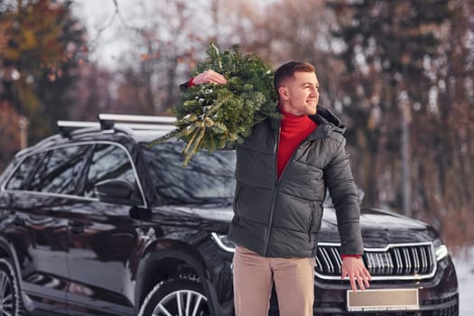 Holding green fir in hands. Man is outdoors near his car. Conception of holidays.