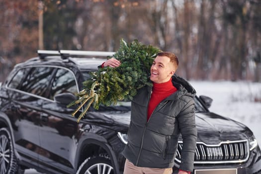 Holding green fir in hands. Man is outdoors near his car. Conception of holidays.
