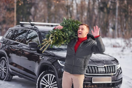 Holding green fir in hands. Man is outdoors near his car. Conception of holidays.
