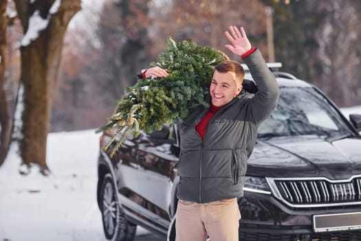 Holding green fir in hands. Man is outdoors near his car. Conception of holidays.