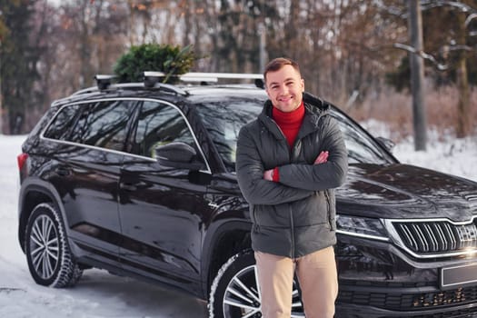 Front view. Man with little green fir is outdoors near his car. Conception of holidays.