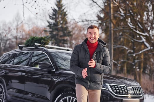 Front view. Man with little green fir is outdoors near his car. Conception of holidays.