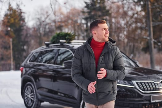 Man with little green fir is outdoors near his car. Conception of holidays.