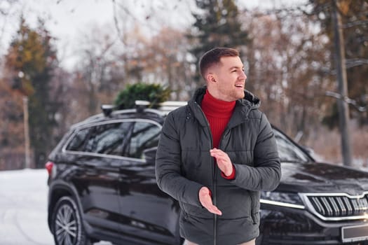 Man with little green fir is outdoors near his car. Conception of holidays.