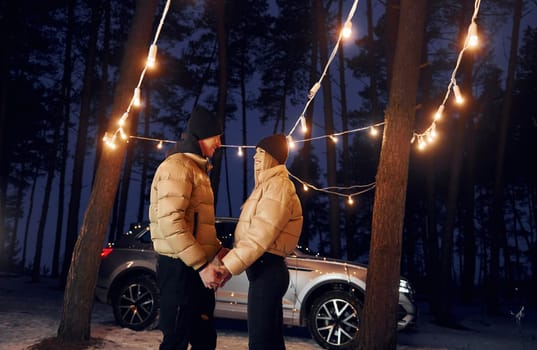 Holding by the hands. Couple standing in the forest and celebrating New year.